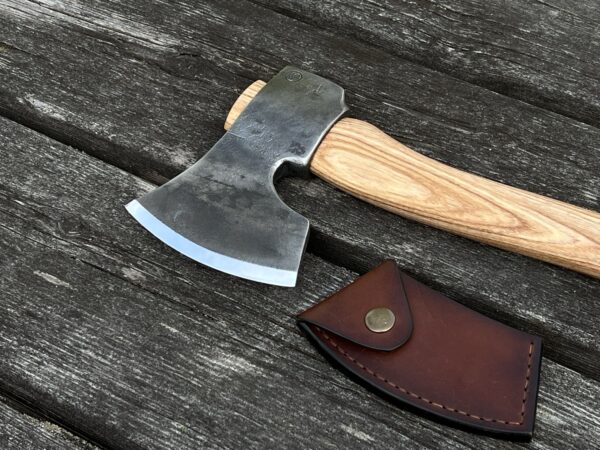 The Sloyd carving axe hand-forged for spoon carving and green woodworking with a sheath on a table